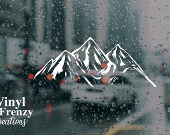 May include: White vinyl decal of a mountain range silhouette on a blurry background of a rainy city street. The decal is for a car window or other smooth surface. The text "Vinyl Frenzy Creations" is at the bottom of the image.