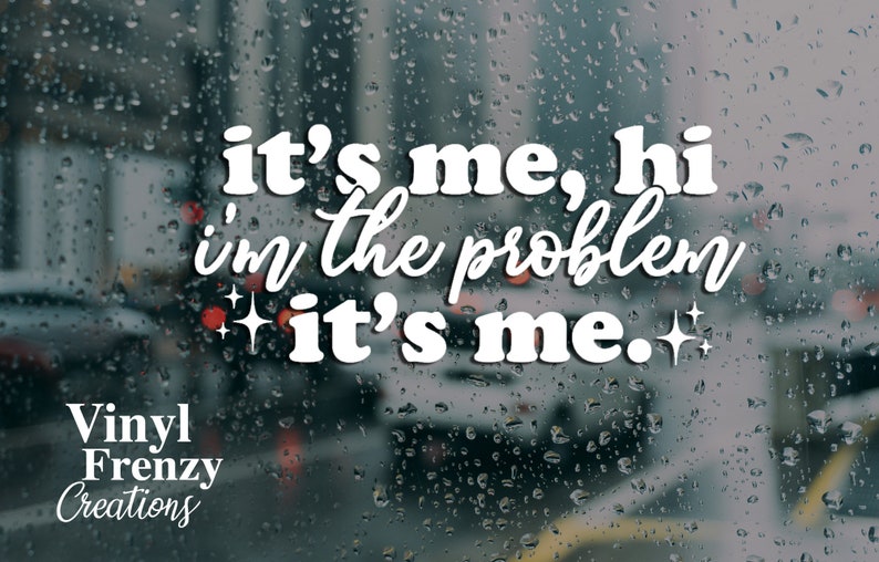 May include: White vinyl decal with the text "it's me, hi i'm the problem it's me." with two small stars on either side of the text. The decal is on a blurry background of a car window with raindrops.