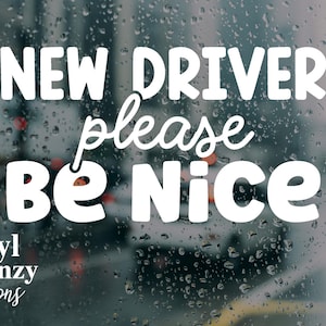 Puede incluir: Un adhesivo de vinilo blanco aplicado sobre una ventana con gotas de lluvia que muestra el texto NEW DRIVER please BE Nice en una mezcla de fuentes sans-serif y script. En la esquina inferior izquierda aparece Vinyl Frenzy Creations.