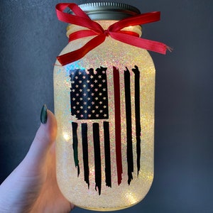 May include: A glass jar with a red ribbon tied around the lid. The jar is filled with glitter and has a black and red American flag design on the front.