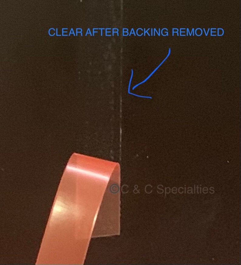 May include: A close-up of a clear adhesive tape with a pink backing. The backing has been partially removed, revealing the clear adhesive. The text "CLEAR AFTER BACKING REMOVED" is visible in the top right corner of the image.