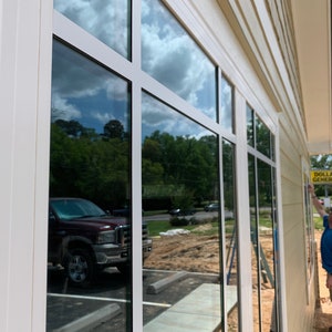 May include: A white building with large windows reflecting the sky and a truck parked outside. A yellow sign with the text "Dollar General" is visible on the right side of the building.