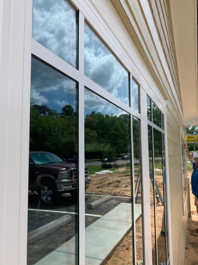 May include: A white building with large windows reflecting the sky and a truck parked outside. A yellow sign with the text "Dollar General" is visible on the right side of the building.