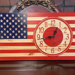 May include: A wooden American flag clock with a red, white and blue colour scheme. The clock face is a red circle with white numbers and black hands.