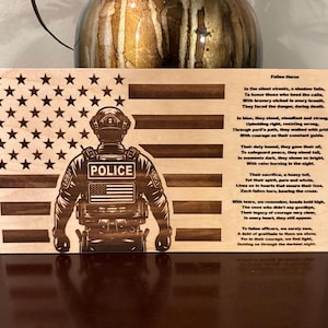 May include: A wooden plaque with an American flag design and a silhouette of a police officer. The plaque features a poem about fallen heroes, with the text "Fallen Heroes" at the top.
