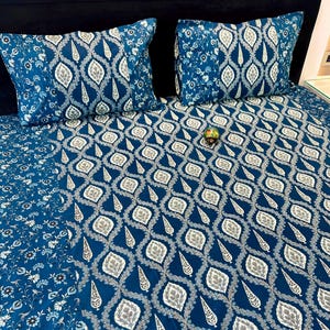 Peut inclure: Un ensemble de literie bleu comprenant une housse de couette et deux taies d'oreiller assorties. Le motif répété présente des formes de gouttes blanches et grises et des motifs floraux. L'ensemble est en tissu doux.