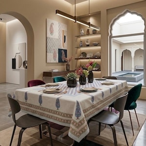 Può includere: Un tavolo da pranzo rettangolare coperto da una tovaglia color crema con un motivo paisley blu e rosa, apparecchiato con piatti, posate e tre vasi scuri contenenti piante grasse e fiori rosa, circondato da sei sedie moderne.