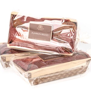 May include: Three loaves of pumpkin bread wrapped in clear plastic and placed in brown paper boxes with a brown and gold pattern. The top loaf has a label that reads "Briarstone Bakery Pumpkin Bread".