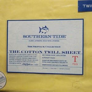 May include: A yellow label with the text "Southern Tide" and "The Skipjack Collection" in black. The label also features a blue fish logo and the text "The Cotton Twill Sheet" in black. The label also includes details about the sheet, such as the thread count, fabric type, and size. The label is on a yellow background with the word "Twin" in blue.