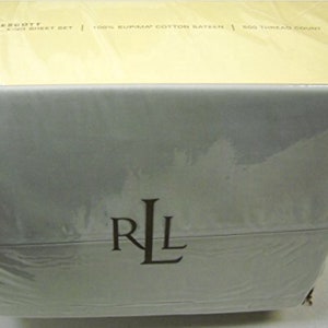 May include: A white box with a yellow top. The box is wrapped in plastic and has the Ralph Lauren logo on the front. The text on the box reads "PRESCOTT CAL KING SHEET SET | 100% SUPIMA COTTON RATEEN | 500 THREAD COUNT".