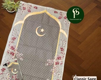 May include: Classic Sage prayer mat with a floral pattern in red and white. The mat features a gold-colored arch design with a crescent moon and star. A matching carrying bag is included. The text "Classic Sage" is visible.
