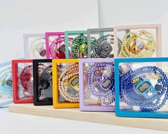 May include: A collection of prayer beads in various colors, each displayed in a clear, square frame. The beads are arranged in a circular pattern, with a digital counter in the center. The frames are in shades of pink, blue, green, and yellow.
