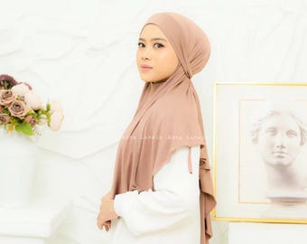May include: Mauve colored jersey hijab with a gathered design. The hijab is worn by a person with a white shirt.