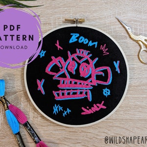 May include: A black embroidery hoop with a pink and blue skull design. The design includes the words "Boom", "Ha Ha", and "Sink".