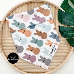 May include: White tie-on bandana with a colorful bunny pattern. The bandana has the text "Hazel Pup Designs" on the bottom right corner.