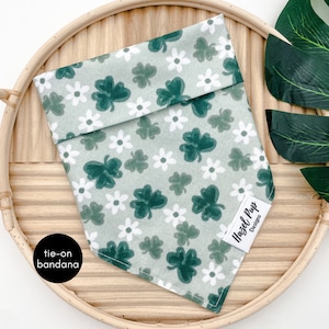 Op de afbeelding: Groen-witte strikbandana met een klavertjevier- en bloemenpatroon. De bandana heeft een label met de tekst "Hazel Pup Designs".