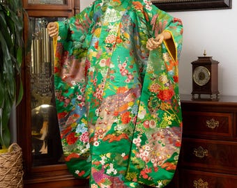Può includere: Un vivace kimono verde con un colorato motivo floreale e di piume di pavone. L'indumento presenta maniche lunghe con finiture gialle ed è esposto su un manichino. Il kimono è un tradizionale capo giapponese.