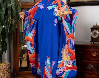 Könnte beinhalten: Ein leuchtend blauer Kimono mit farbenfrohen Mustern an Ärmeln und Saum. Das Design weist rote, orangefarbene, violette und türkisfarbene Akzente auf. Der Kimono wird auf einer Schaufensterpuppe präsentiert, die seine fließende Silhouette und die aufwendigen Kunstwerke zeigt.