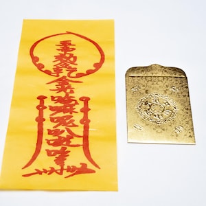 May include: A yellow paper with red Chinese characters and a gold envelope with an embossed floral design. The paper has vertical text and a circular design at the top. The envelope has a decorative flap.