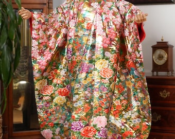 Könnte beinhalten: Ein traditionelles japanisches Kimono mit einem goldenen, rosa und grünen Blumenmuster. Das Kimono ist aus einem luxuriösen Stoff mit schimmerndem Finish gefertigt.