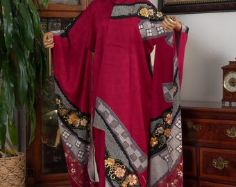 May include: A vibrant red kimono with decorative patterns of flowers, houses, and geometric shapes. The kimono is displayed on a mannequin. The sleeves are long and flowing, and the design includes black, gold, and gray accents. The garment is a traditional Japanese style.