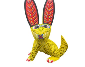 May include: A hand-painted wooden rabbit figurine. The rabbit is primarily yellow with black markings, red and yellow striped ears, and red accents on its paws. The rabbit has blue and white eyes and a red and blue star on its chest.