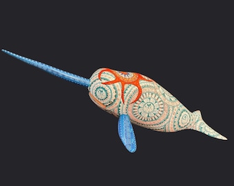 May include: A decorative narwhal sculpture with a long, blue tusk and patterned body. The body features intricate teal and coral designs, with a coral-colored starfish-like shape on its back. The fins are blue, and the background is dark.