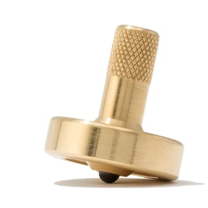 Puede incluir: Una peonza de metal de color dorado con una parte superior texturizada y un rodamiento negro.