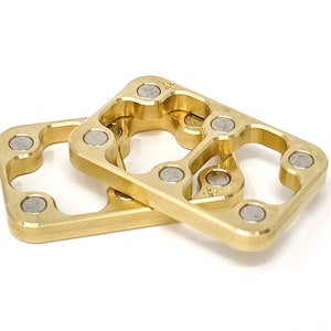 May include: Two gold-coloured metal squares with rounded edges and four small silver circles on each side. The squares are stacked on top of each other.