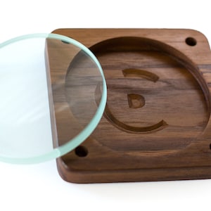 May include: A wooden box with a circular cutout and a glass lid. The cutout is shaped like the letter "E".