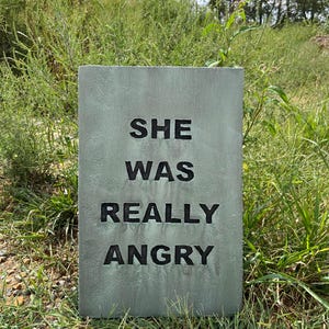 May include: A green tombstone with the words "SHE WAS REALLY ANGRY" written in black.