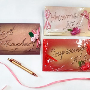 May include: Three handmade cards with pink and red ribbon accents. The cards have gold lettering that reads "Best Teacher", "You're Number 1", and "Supermom Number 1".