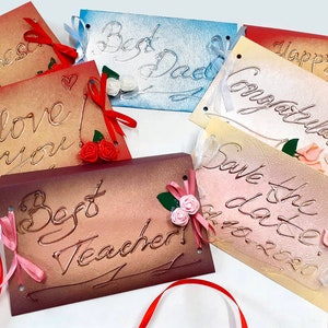 May include: Six handmade cards with different messages and embellishments. The cards are made of textured paper and have a vintage look. The messages include "I love you", "Best Dad", "Happy Anniversary", "Congratulations", "Save the Date", and "Best Teacher".