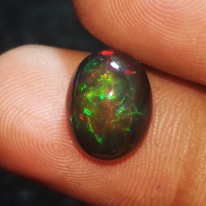 May include: A dark green and black oval opal gemstone with red and green flashes of color.