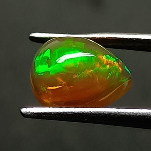 Può includere: Una pietra preziosa di opale verde a forma di lacrima con una base dorata, tenuta da una pinzetta.