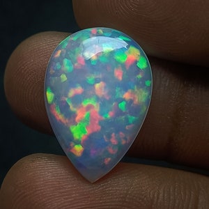 May include: A teardrop-shaped opal cabochon with a white base and iridescent green, blue, and pink flashes.