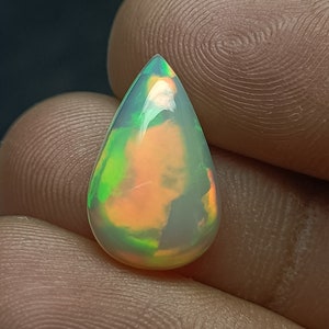 May include: A teardrop-shaped opal gemstone with a green, orange, and white iridescent sheen.