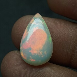 May include: A teardrop-shaped opal gemstone with a milky white base and iridescent flashes of pink, green, and blue.