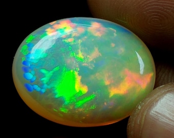 May include: A white oval opal gemstone with green, blue, and orange iridescent flashes.