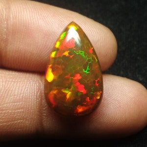 May include: A teardrop-shaped opal gemstone with a brown base and flashes of red, green, and yellow.