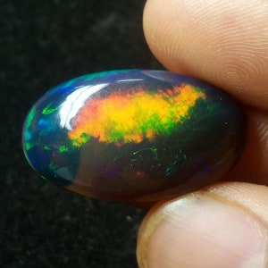 Könnte beinhalten: Ein schwarzer Opal-Edelstein mit einem Regenbogen aus Farben, darunter Grün, Gelb, Orange und Rot.