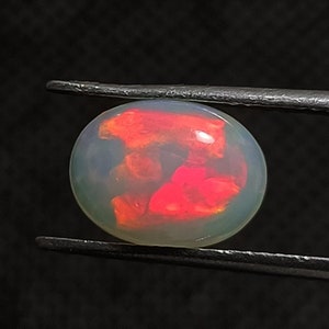 May include: A round, opaque opal gemstone with a white base and red and orange flashes of color.