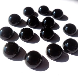 May include: A collection of 13 black cabochon gemstones, each with a smooth, polished surface. The stones are arranged in a scattered pattern on a white background.