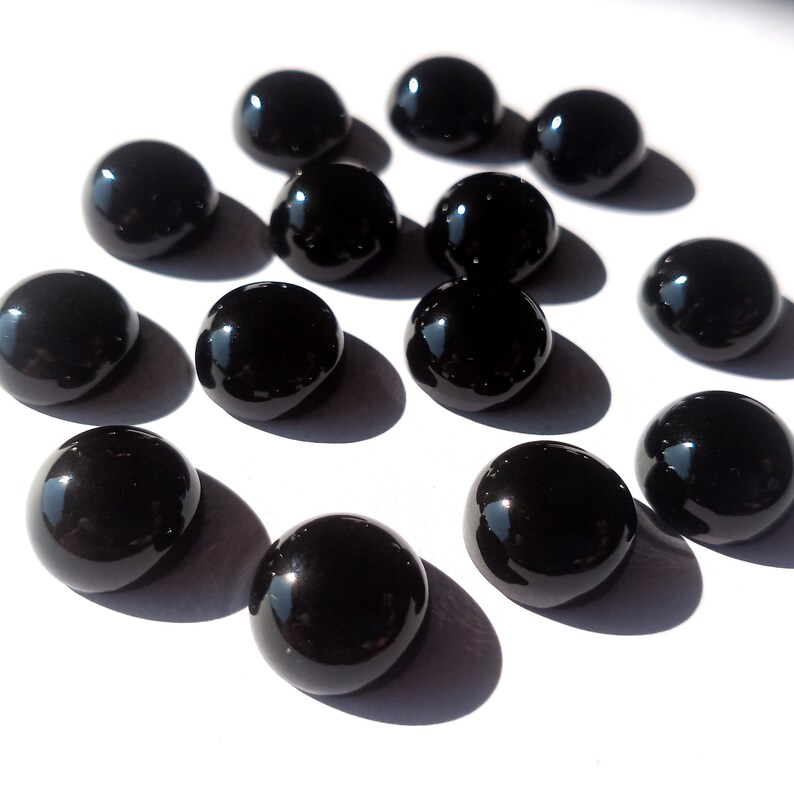 May include: A collection of 13 black cabochon gemstones, each with a smooth, polished surface. The stones are arranged in a scattered pattern on a white background.