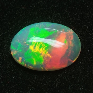 May include: Oval-shaped opal gemstone with a white base and iridescent flashes of green, yellow, and red.