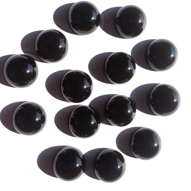 May include: A collection of 14 black glass spheres, each with a smooth, reflective surface. The spheres are arranged in a circular pattern on a white background.