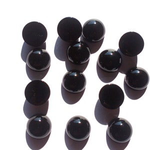 May include: A collection of 13 black round cabochon gemstones. The gemstones are smooth and shiny.