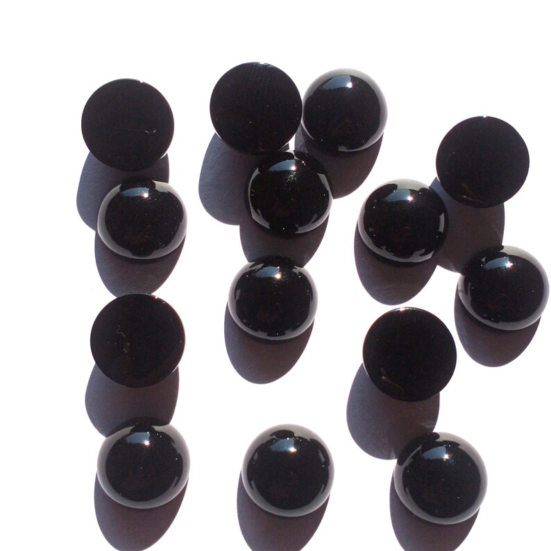 May include: A collection of 13 black round cabochon gemstones. The gemstones are smooth and shiny.
