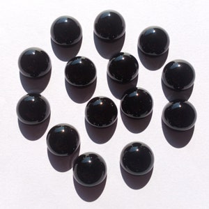 May include: A collection of 14 black cabochon gemstones, each with a smooth, polished surface. The stones are arranged in a circular pattern on a white background.
