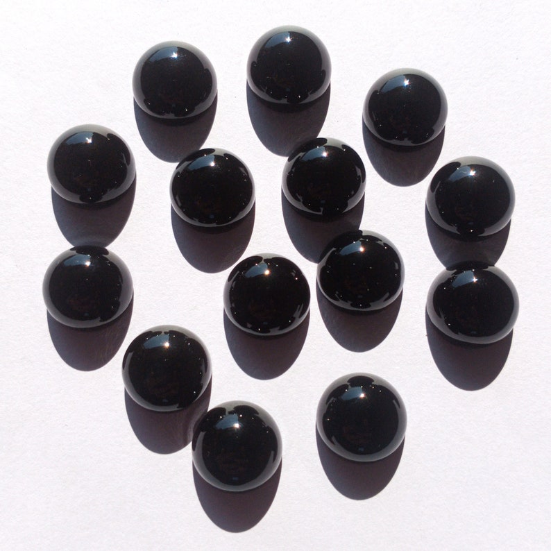 May include: A collection of 14 black cabochon gemstones, each with a smooth, polished surface. The stones are arranged in a circular pattern on a white background.